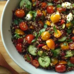 Colorful Italian quinoa salad in a white bowl with fresh vegetables, mozzarella, and a lemon garlic vinaigrette drizzle.